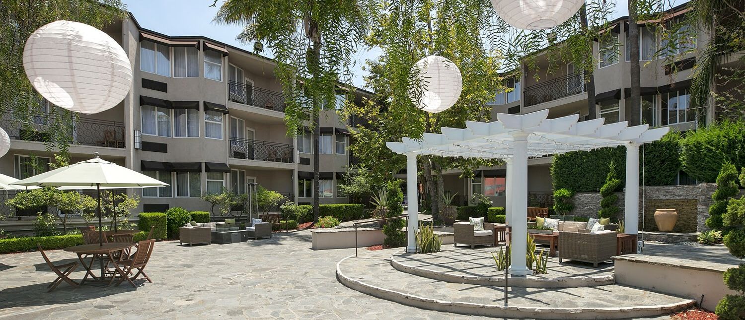 A sunny hotel courtyard with white lanterns, outdoor seating, and a shaded gazebo area.