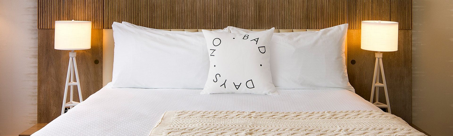 A neatly made bed with white sheets and pillows, a decorative pillow in the center, and two matching bedside lamps on either side.
