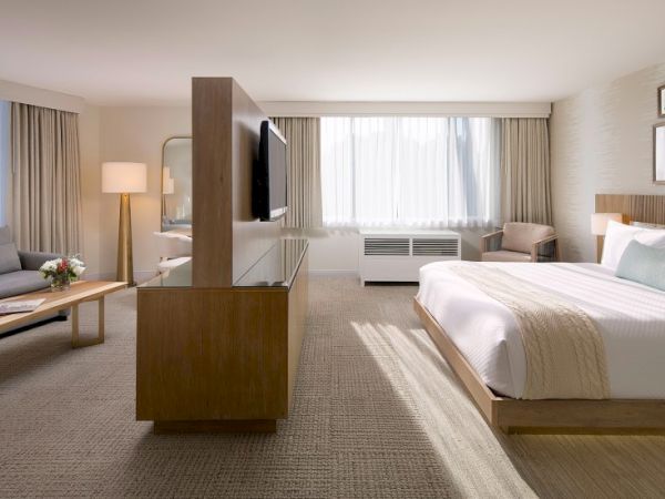 A spacious hotel room with a king bed, seating area, desk, full-length curtains, and a large window letting in natural light.