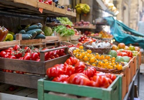 A bustling outdoor market with crates of colorful tomatoes, peppers, and other fresh produce on display for shoppers.