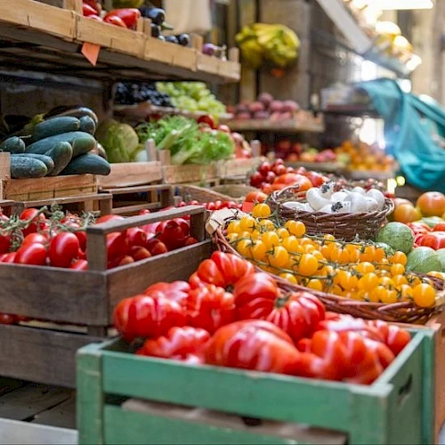 A bustling outdoor market with crates of colorful tomatoes, peppers, and other fresh produce on display for shoppers.