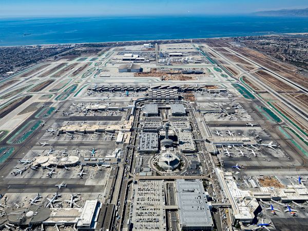 Aerial view of a large airport complex with runways, terminals, taxiways, and surrounding desert terrain near the coast.
