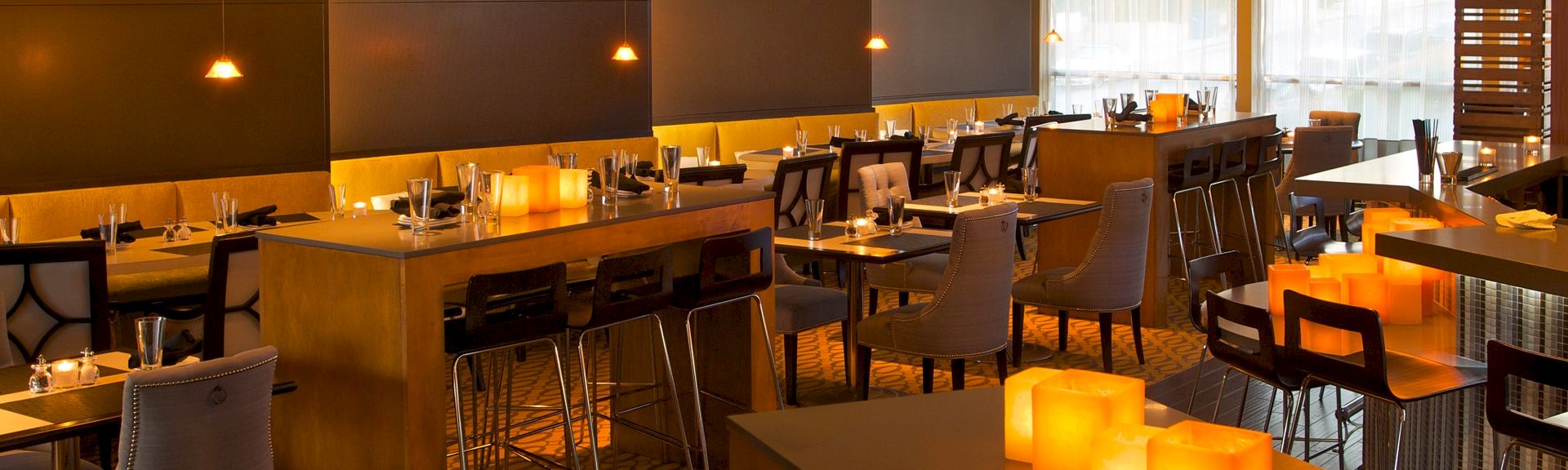 A modern, warmly lit restaurant with wooden tables, cushioned chairs, and glowing candlelit decor creating an intimate ambiance.