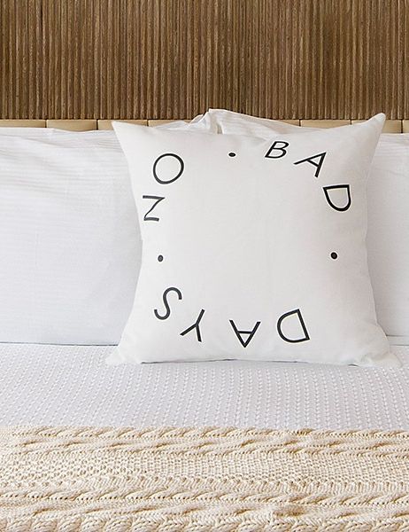 A neatly made bed with white linens, two bedside lamps, a decorative pillow, and a cozy knit throw at the foot, in a calm hotel room vibe.