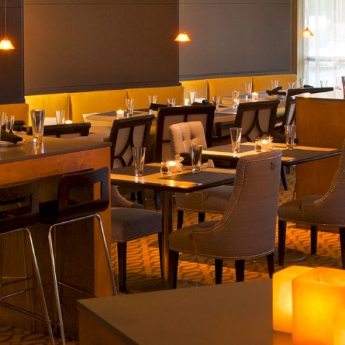 A stylish dimly lit restaurant with warm candlelight, modern seating, wooden counters, and tables set with glassware and cutlery.