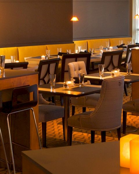 A stylish dimly lit restaurant with warm candlelight, modern seating, wooden counters, and tables set with glassware and cutlery.