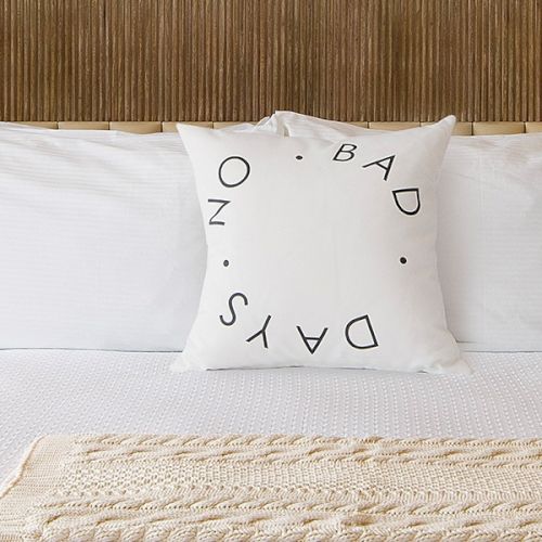 A neatly made hotel bed with white linens, two bedside lamps, a decorative pillow, and a knitted throw at the foot.