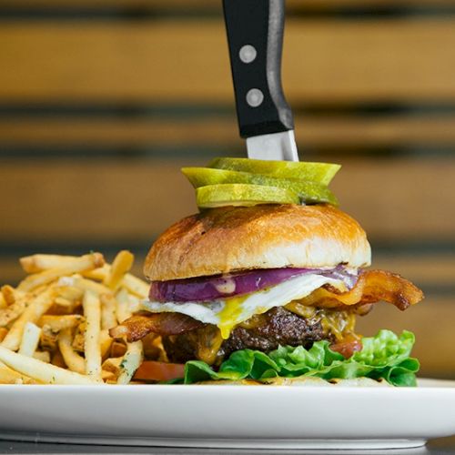 A juicy burger with melted cheese, crispy onions, lettuce, tomato, and sauce stacked in a toasted bun.