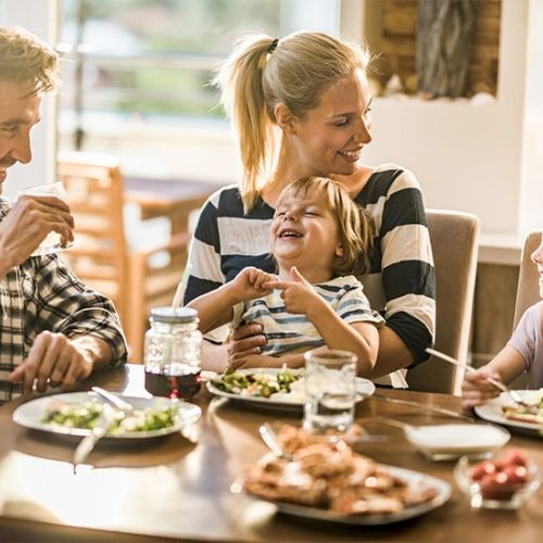 A family dinner scene with kids and adults sharing food around a table, smiling and chatting together.