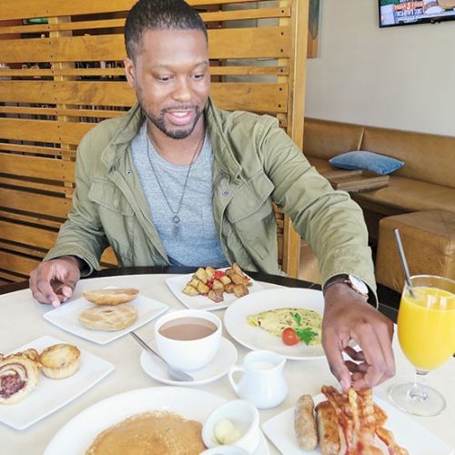 A man sits at a table with breakfast items, including orange juice and toast, in a casual dining setting. Top it at 140 characters, always ending the sentence.
