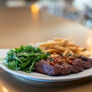 Crispy fried meat with greens and a lemon wedge on a white plate, set on a dark table with warm bokeh lights in the background.