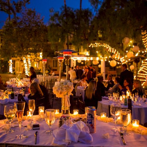 A lively outdoor dinner party at night with fairy lights, candlelit tables, and guests enjoying a festive, romantic courtyard setting.