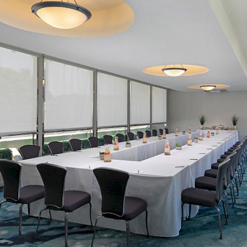 A long conference table with white tablecloths and chairs, set in a bright, windowed meeting room with round ceiling lights.